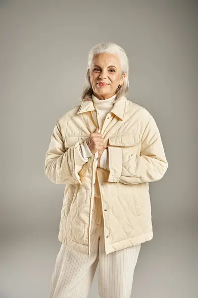 Hermosa y gris mujer de mediana edad en traje elegante posando sobre fondo gris - foto de stock