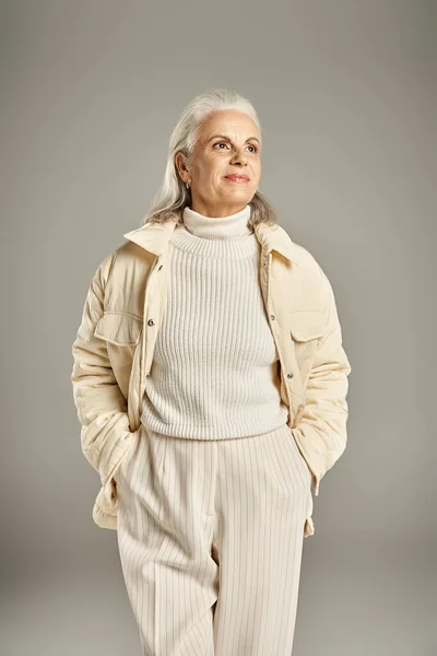 Beautiful and grey haired middle aged woman in elegant attire posing on grey background — Stock Photo