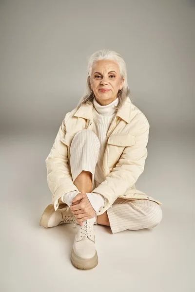 Beautiful and grey haired middle aged woman in elegant attire posing on grey background — Stock Photo
