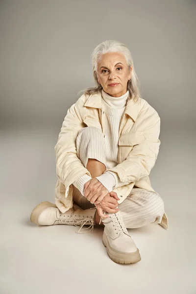 Beautiful and grey haired middle aged woman in elegant attire posing on grey background — Stock Photo