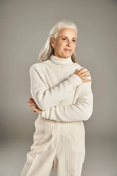 Schöne und grauhaarige Frau mittleren Alters in eleganter Kleidung posiert auf grauem Hintergrund — Stockfoto