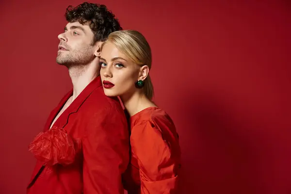 Blonde woman with red lips leaning on shoulder of man in vibrant attire of red background, fashion — Stock Photo
