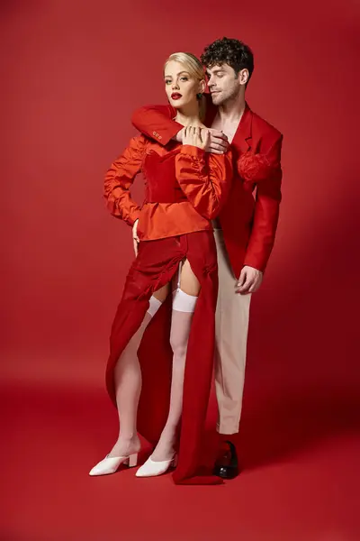 Comprimento total de homem bonito abraçando mulher em traje elegante no fundo vermelho, casal elegante — Fotografia de Stock