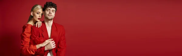 Bella giovane donna con i capelli biondi e le labbra rosse che abbracciano l'uomo in abbigliamento elegante su rosso, banner — Foto stock
