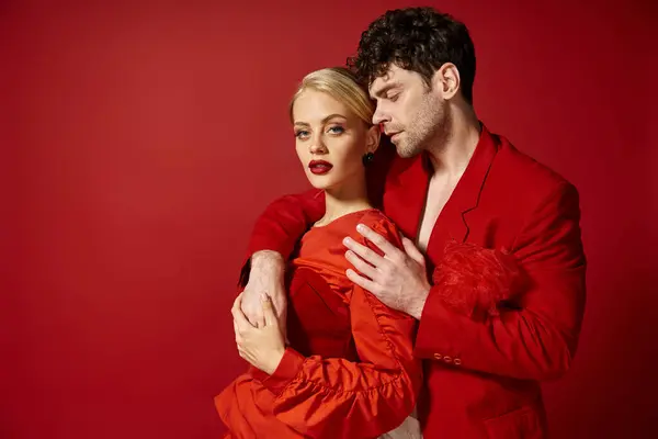 Hombre guapo poniendo la mano alrededor del cuello de la mujer rubia bonita con labios rojos en el telón de fondo vibrante - foto de stock