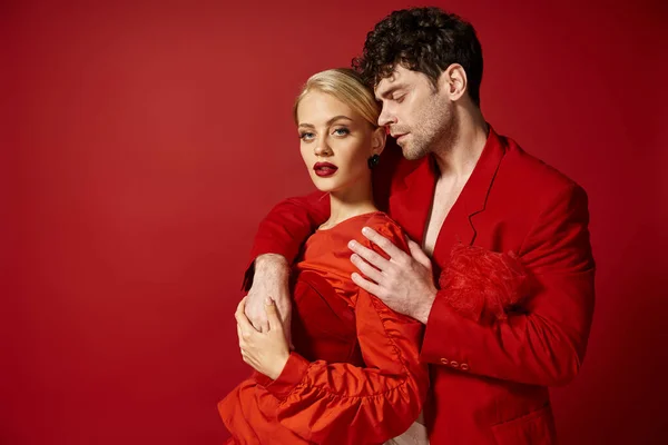 Handsome man putting hand around neck of pretty blonde woman with red lips on vibrant backdrop — Stock Photo