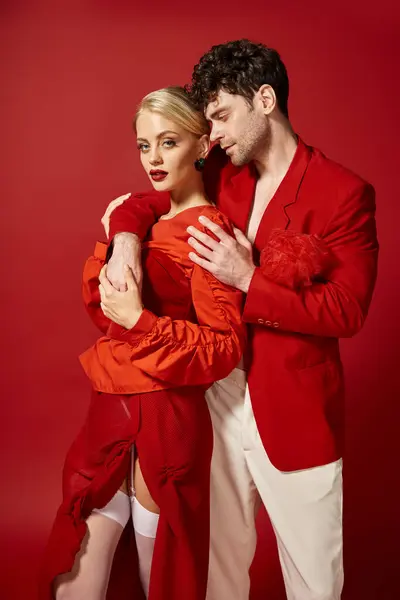 Schöner Mann legt die Hand um den Hals einer blonden Frau mit roten Lippen vor lebendigem Hintergrund, Mode — Stockfoto