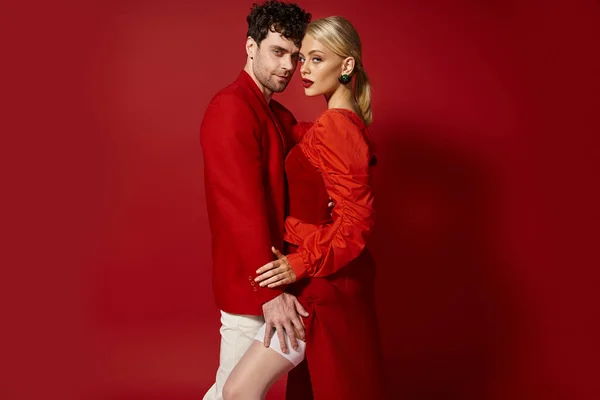 Handsome man touching leg of seductive blonde woman in sexy white stockings on red background — Stock Photo