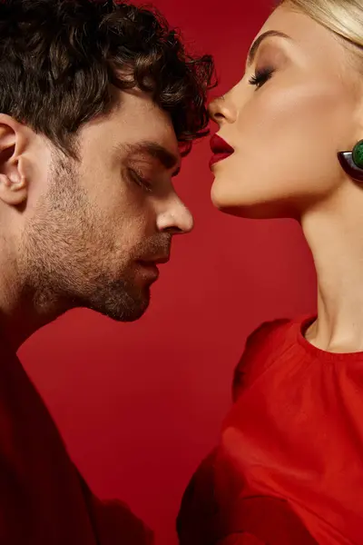 Vista lateral do homem bonito posando com bela mulher loira com lábios vermelhos no fundo vibrante — Fotografia de Stock