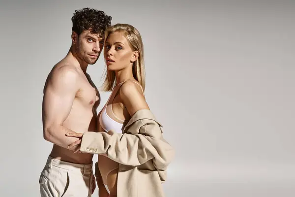 Hemdloser Mann posiert mit attraktiver und blonder Frau in Body und Blazer auf grauem Hintergrund — Stockfoto