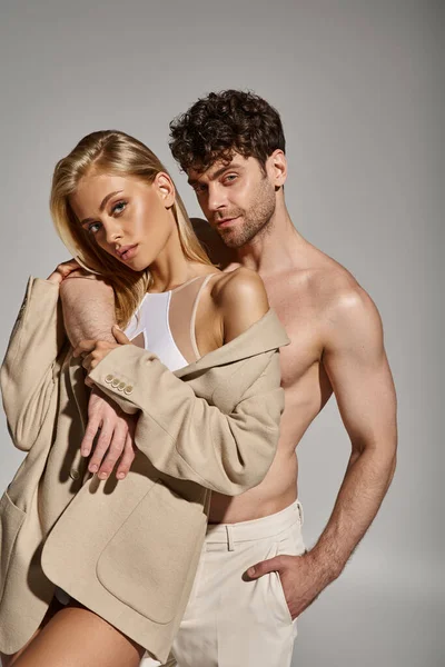 Hemdloser Mann posiert mit der Hand in der Tasche einer weißen Hose neben charmanter Frau im Body mit Blazer — Stockfoto