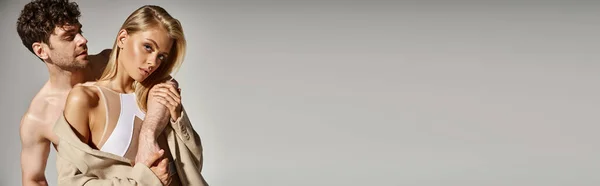 Homem sem camisa posando com mulher bonita em bodysuit e elegante blazer bege no fundo cinza, banner — Fotografia de Stock
