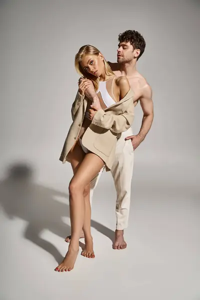 Homme pieds nus posant avec la main dans la poche de pantalon blanc près de jolie femme en body avec blazer — Photo de stock
