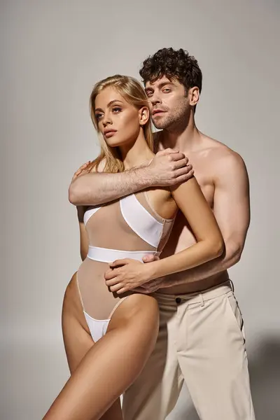 Без сорочки чоловік з м'язистим тілом обіймає красиву молоду жінку на сірому фоні, сексуальна пара — стокове фото