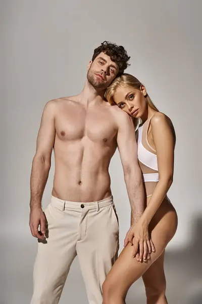 Без сорочки чоловік з м'язистим тілом тримає руку красивої блондинки на сірому фоні, сексуальна пара — стокове фото