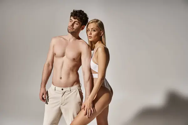 Shirtless man with muscular body holding hand of blonde woman on grey background, sexy couple — Stock Photo