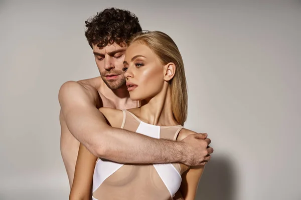 Leidenschaftlicher Mann mit hemdlosem Körper verführt hübsche Frau im Body auf grauem Hintergrund, sexy Paar — Stockfoto
