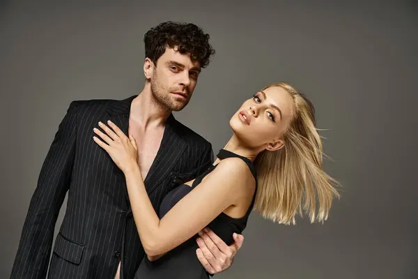 Fashionable couple in elegant evening attire posing together on grey background, man and woman — Stock Photo