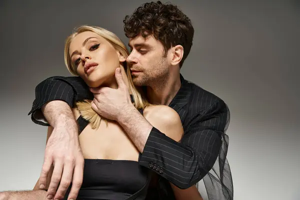 Bel homme en costume de designer rouge posant avec modèle blonde sur fond vibrant, couple branché — Photo de stock