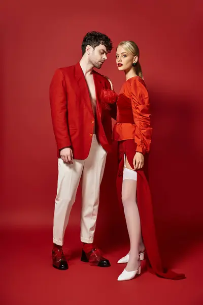 Bell'uomo in abito designer rosso in posa con modella bionda su sfondo vivace, coppia alla moda — Foto stock