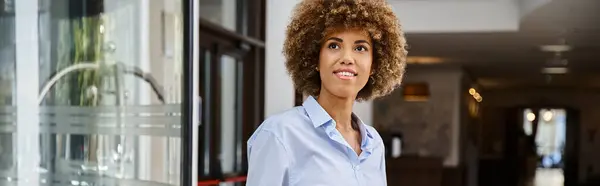 Inteligentemente vestida e feliz mulher americana africana com cabelo encaracolado em pé no lobby do hotel, banner — Fotografia de Stock