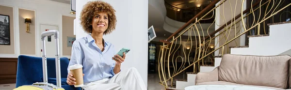 Banner der glücklichen afrikanisch-amerikanischen Frau mit Coffee to go und Smartphone in Hotellobby — Stockfoto