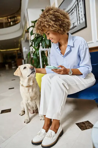 Tourist with phone cuddling dog in pet-friendly hotel, labrador and happy african american woman — Stock Photo