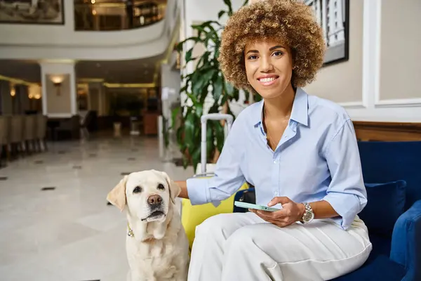 Glücklicher Reisender mit Labrador und Telefon in einem haustierfreundlichen Hotel, Hund und Afroamerikanerin — Stockfoto