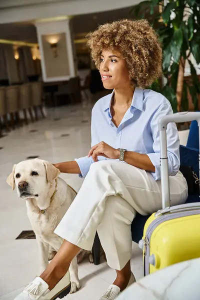 Feliz huésped a la espera de check-in con perro en hotel que acepta mascotas, mujer negra con reloj de pulsera moderno - foto de stock