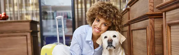 Banner of happy african american woman cuddling dog near suitcase in lobby of pet-friendly hotel — Stock Photo