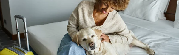 Banner of happy african american woman cuddling labrador near luggage in pet-friendly hotel room — Stock Photo