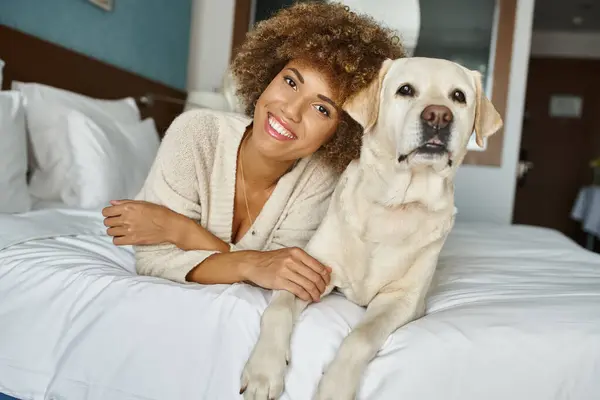 Глибока афроамериканська жінка з її лабрадором лежить на ліжку в готелі, дружній до домашніх тварин, подорожі — стокове фото