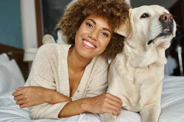 Donna afro-americana positiva con il suo labrador sdraiato su un letto in un hotel pet-friendly, viaggi — Foto stock