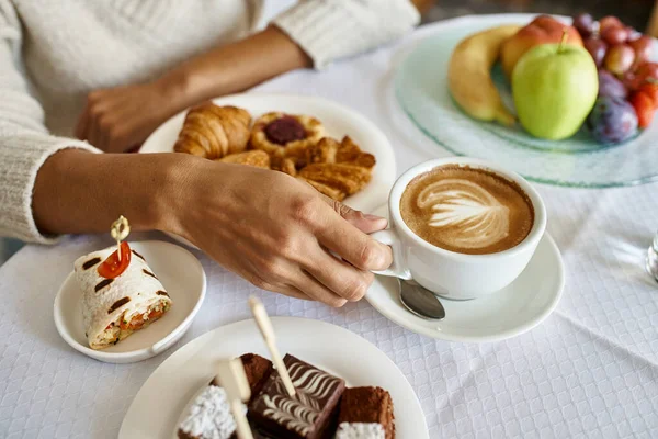 Cropped shot of african american woman enjoying cappuccino and pastries with room service in a hotel — Stock Photo