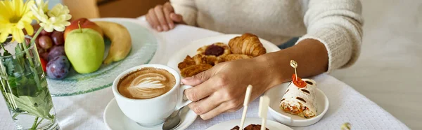 Cropped banner of african american woman enjoying cappuccino and pastries in hotel room — Stock Photo