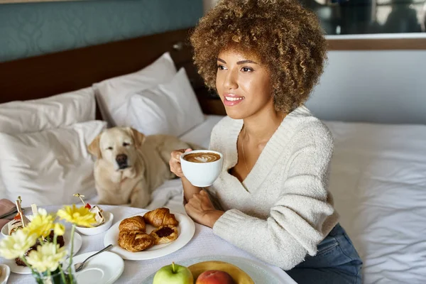 Афроамериканська жінка, насолоджуючись сніданком у номері біля її лабрадору в готелі, дружній до домашніх тварин — стокове фото