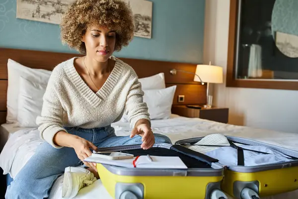 Young African American woman with curly hair unpacking her luggage in hotel room, getaway concept — Stock Photo