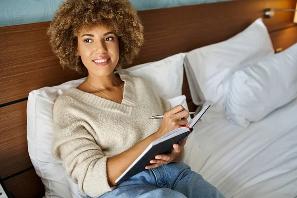 Dreamy and happy African American woman planning her next trip, holding pen and notebook — Stock Photo