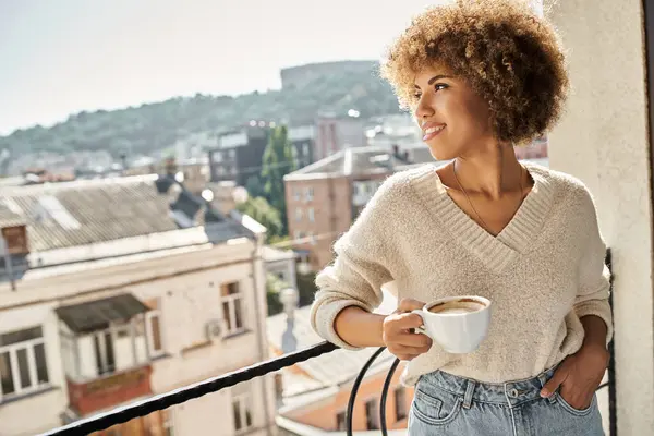 Joyful young african american woman standing with cup of coffee on hotel balcony, city view — Stock Photo