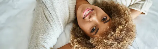 Striscione di felice donna afroamericana sorridente e sdraiata sul letto in camera d'albergo, capovolta — Foto stock