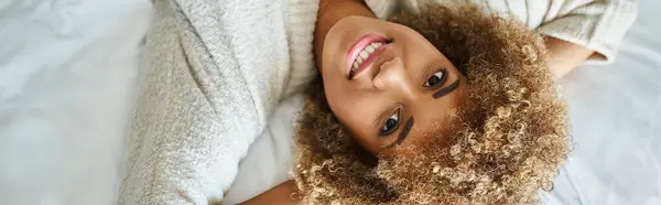 Banner of happy african american woman smiling and lying on bed in hotel room, upside down — Stock Photo