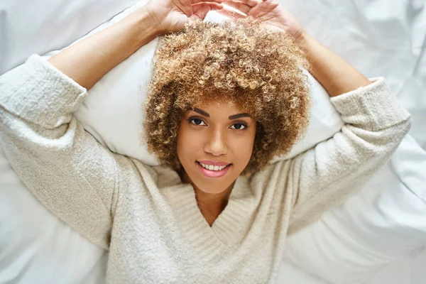 Top view of happy african american woman smiling and lying on bed in cozy hotel room, upside down — Stock Photo