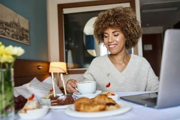Jeune femme afro-américaine utilisant son ordinateur portable près du petit déjeuner à l'hôtel, service en chambre et commodité — Photo de stock