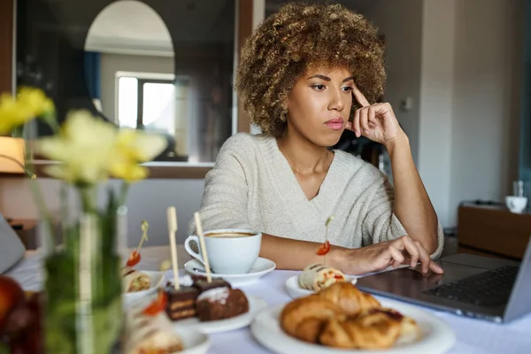 Femme afro-américaine coûteuse utilisant un ordinateur portable près du petit déjeuner à l'hôtel, service en chambre et commodité — Photo de stock