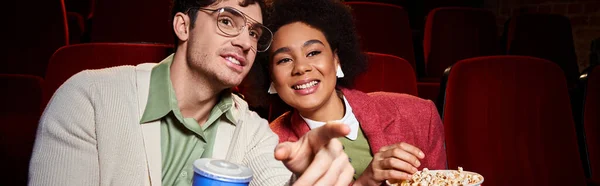 Jolly interracial couple in vibrant attires enjoying movie at cinema on date, Valentines day, banner — Stock Photo