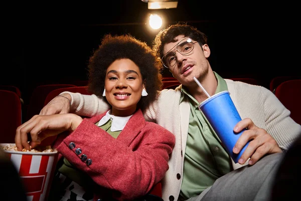 Fröhliches multiethnisches Paar in trendiger Kleidung, das Popcorn teilt und in die Kamera lächelt, Valentinstag — Stockfoto