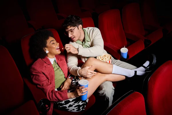 Homem bonito compartilhando pipocas com sua alegre namorada afro-americana no encontro no cinema — Fotografia de Stock