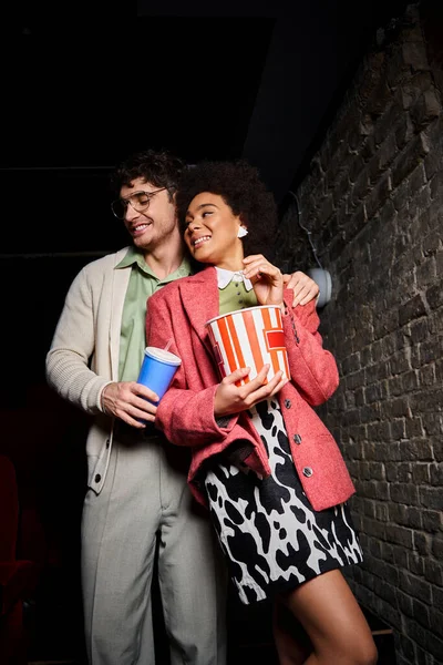 Привлекательная разнообразная пара в модном наряде, улыбающаяся на свидании в кино в день Святого Валентина — стоковое фото