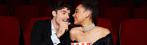 Handsome man sharing popcorn with his pretty african american girlfriend on date at cinema, banner — Stock Photo