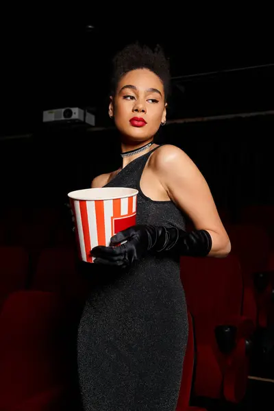 Appealing african american woman with red lipstick posing with popcorn in hands and looking away — Stock Photo